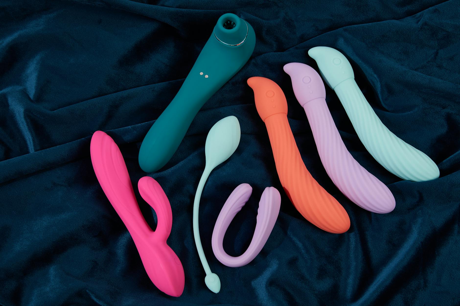 A sleek teal clitoral vibrator on smooth white silk fabric