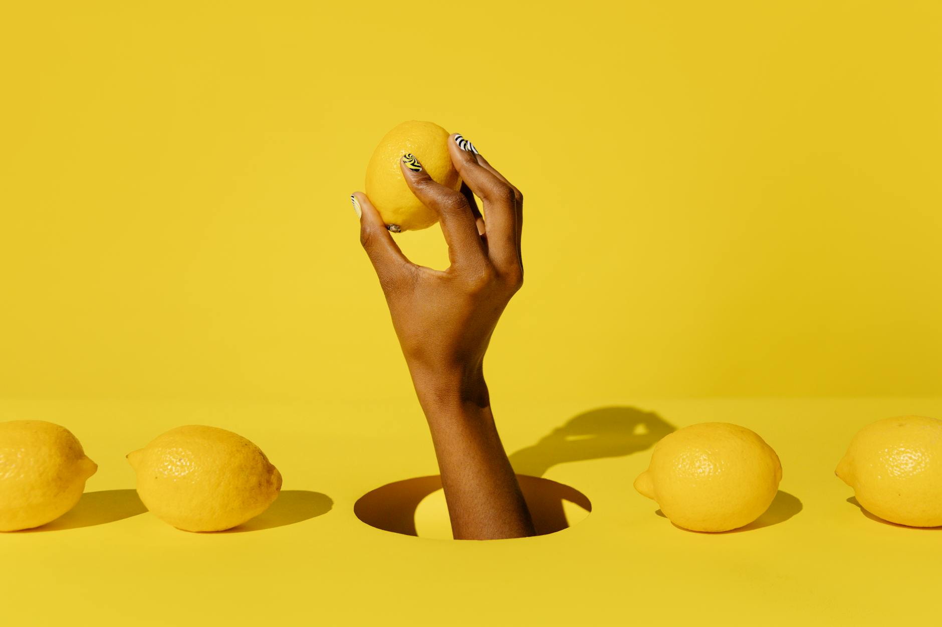 A hand holding a fresh lemon against a vivid yellow background, symbolizing refreshing sensual pleasure