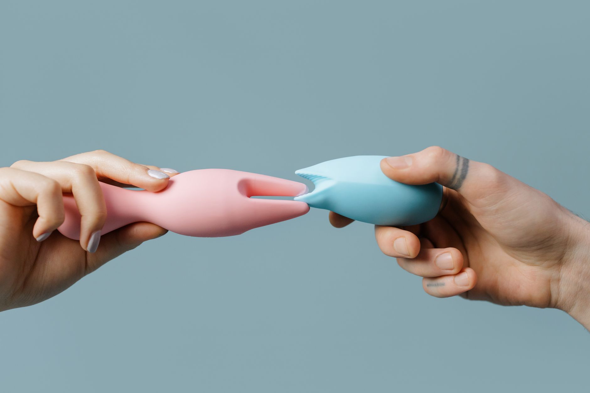 Hands holding pastel-colored silicone vibrators on a soft background