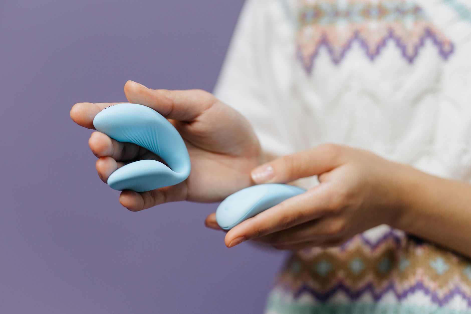 A blue silicone vibrator held in hand against a purple background
