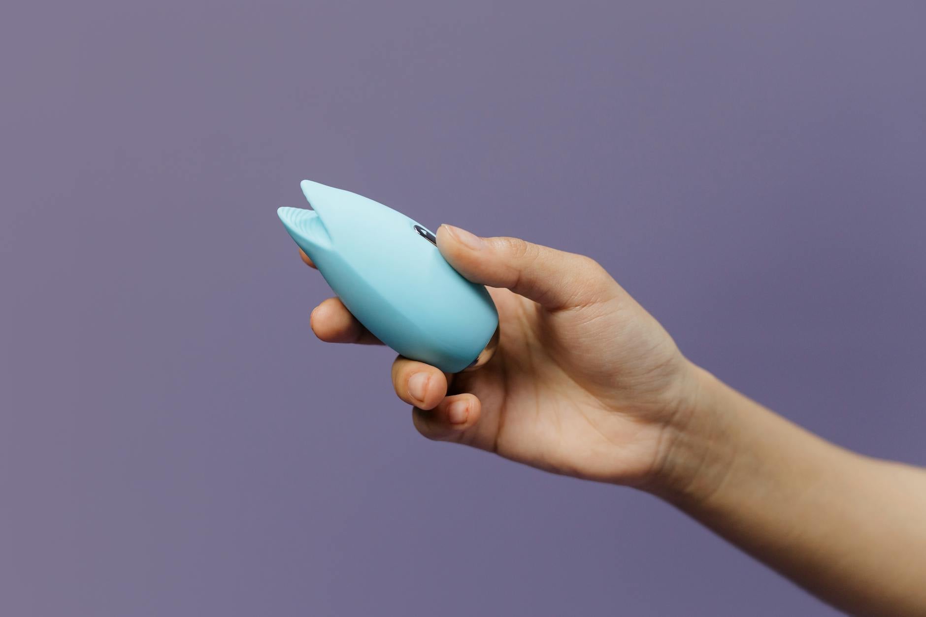 A blue silicone vibrator held in hand against a solid purple background, promoting comfortable self-care and sexuality