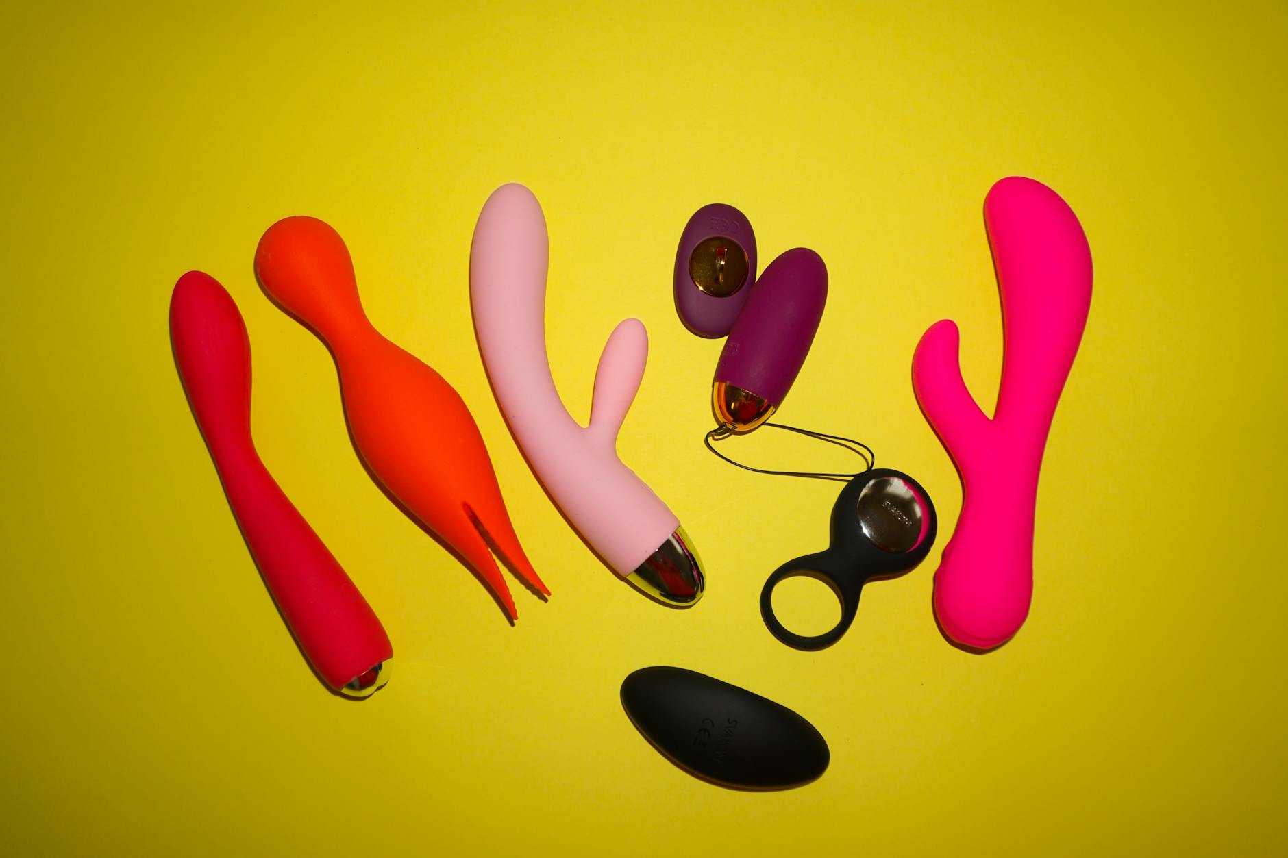 Colorful clitoral vibrators displayed on a bright yellow background, showcasing various shapes and designs